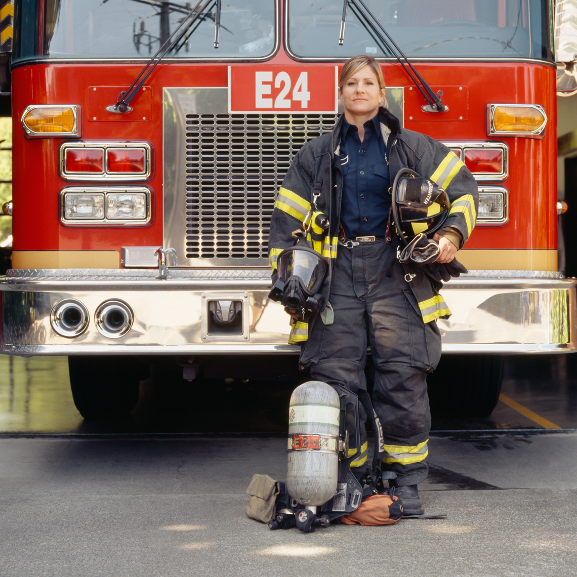 Female woman firefighter with technical gear and fire engine truck. Capable, confident, proud career professional.