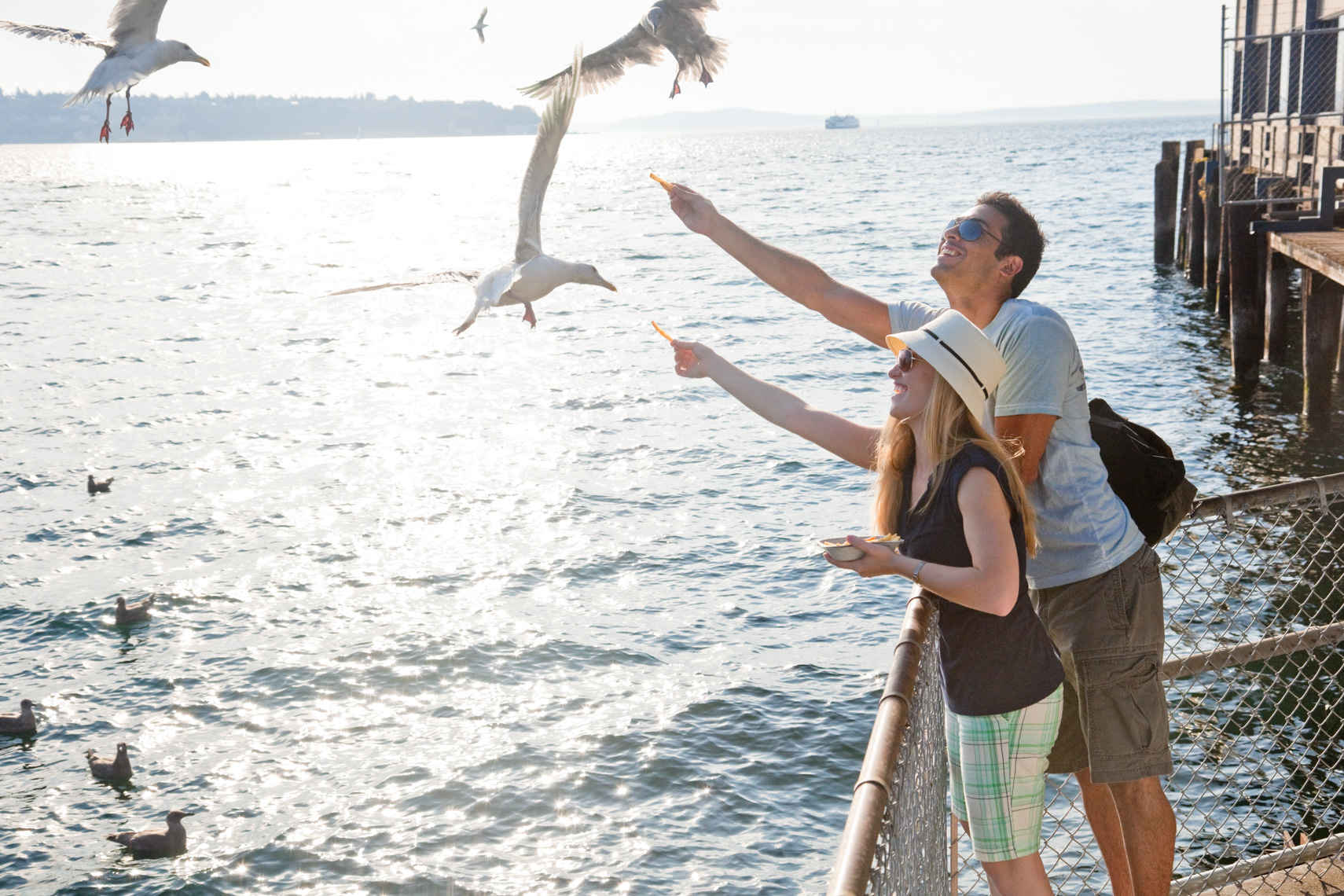 Couple feeding seagulls on Seattle waterfront with harbor scene and ferry in background