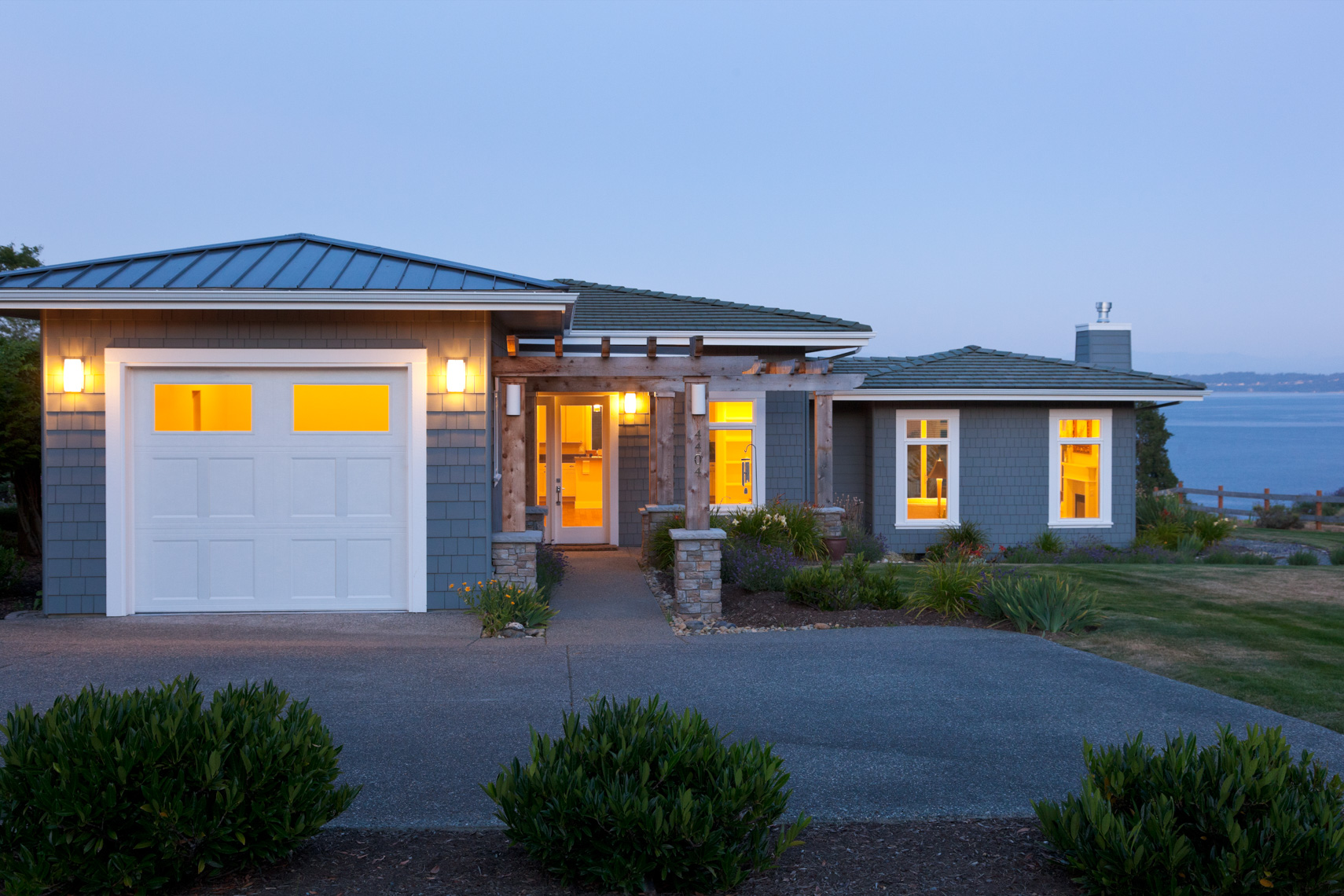 Contemporary house and garage at dusk with exterior lighting and lights on inside. Home energy use, water view real estate.