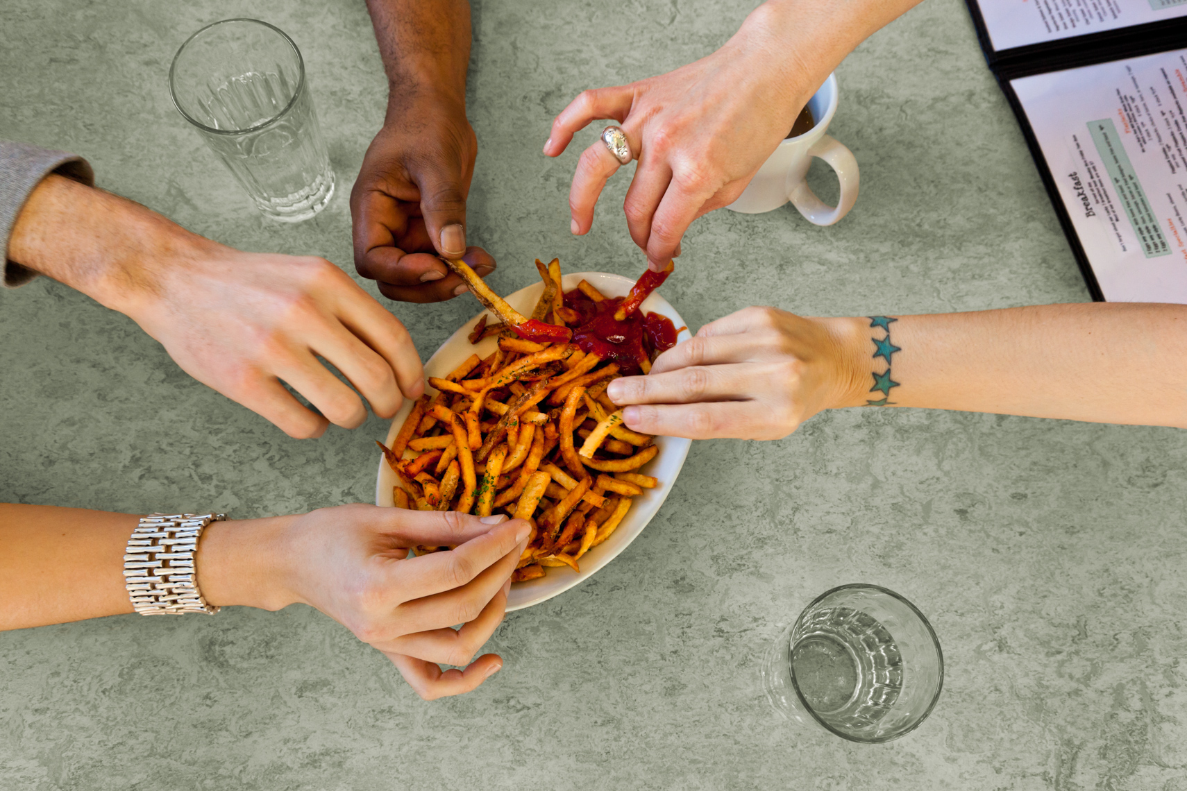 Hands of diverse group of friends eating sharing French fries food in casual restaurant
