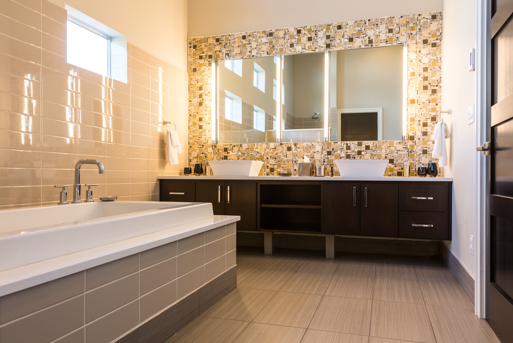 Contemporary upscale, modern home bathroom interior with tile walls and floors, vanity, mirrors, wood cabinets, acrylic soaking tub bathtub and high quality fixtures