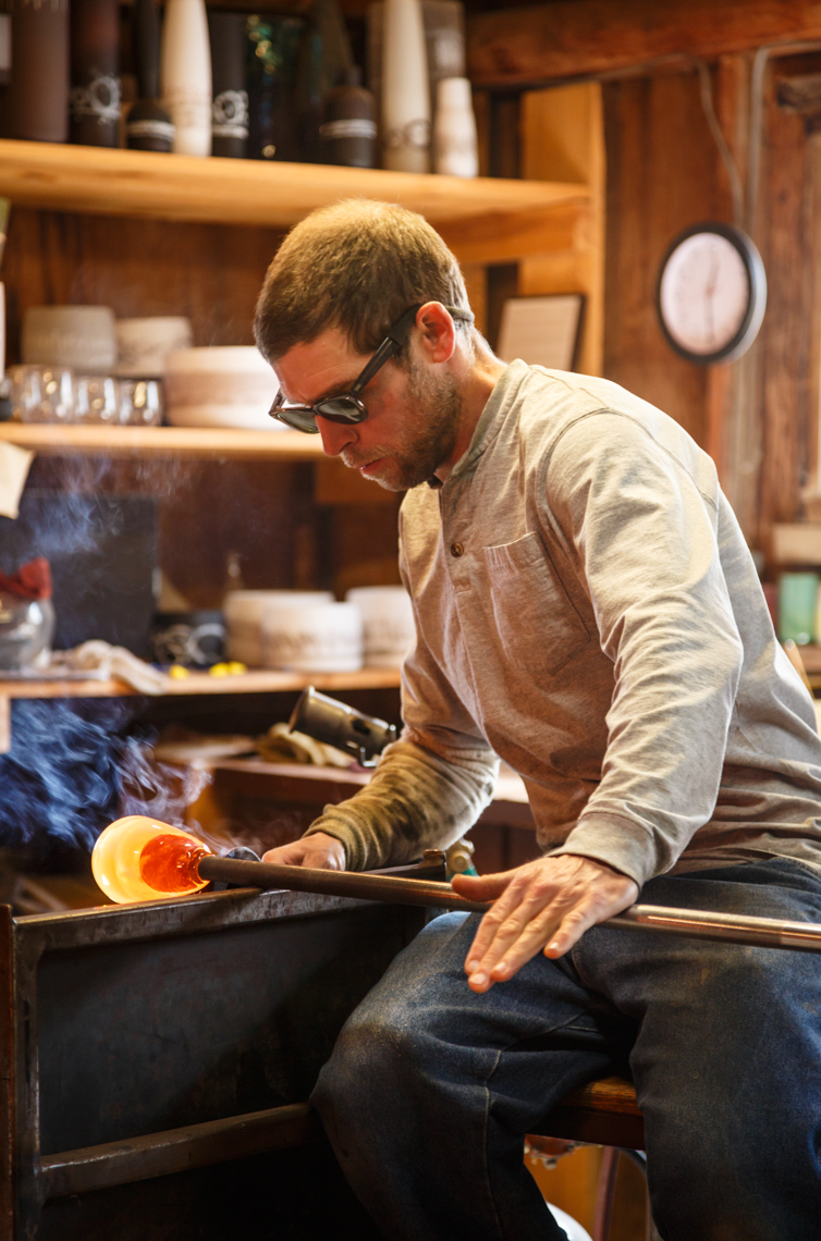 Glassblower artist craftsperson working with hot glass in his studio workshop