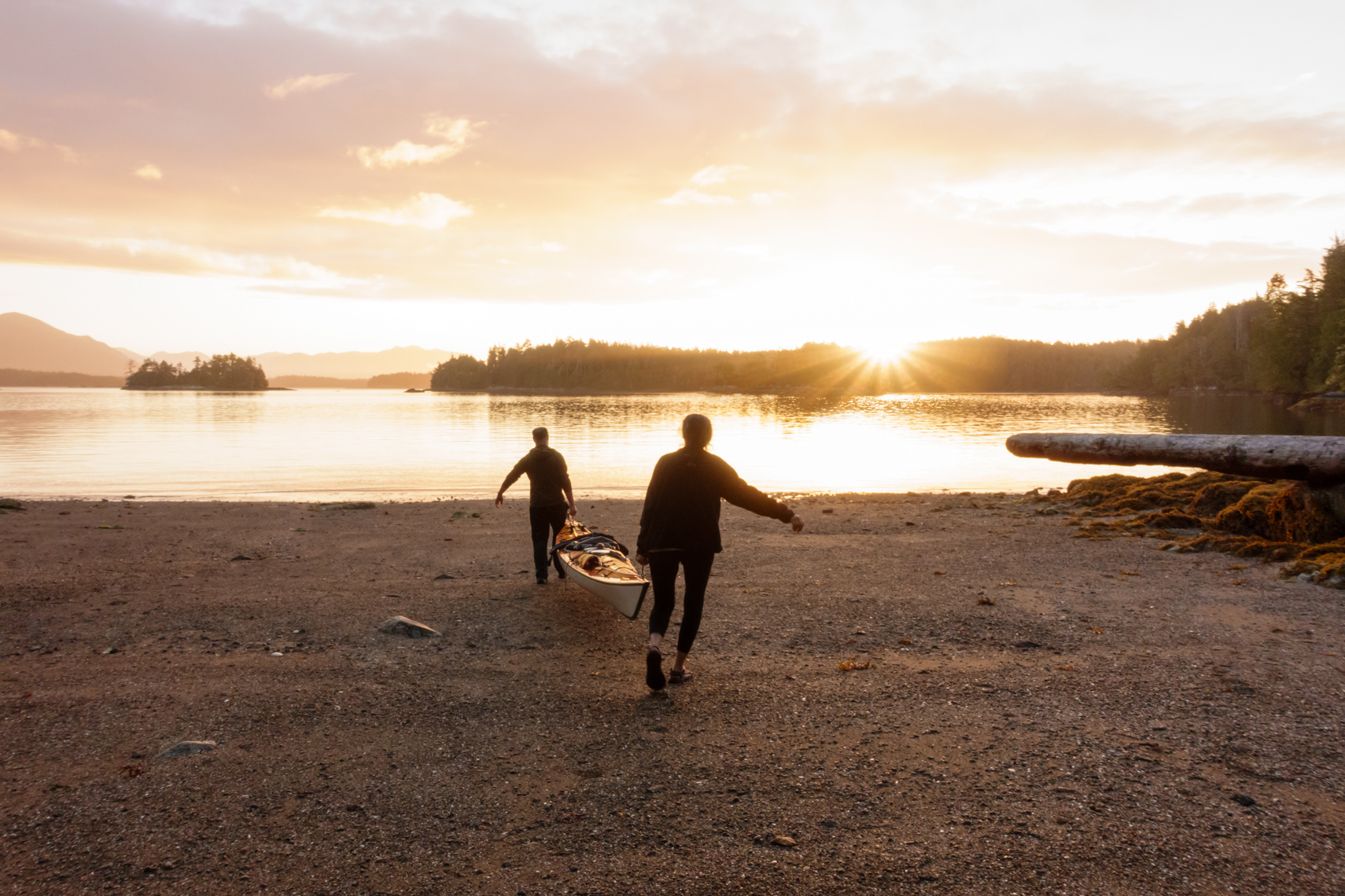People couple carrying launching a sea kayak at sunrise in the remote wilderness, Broken Group Islands, Barkley Sound, Pacific Rim National Park, British Columbia, Canada. Adventure travel teamwork beginnings relationships concept.