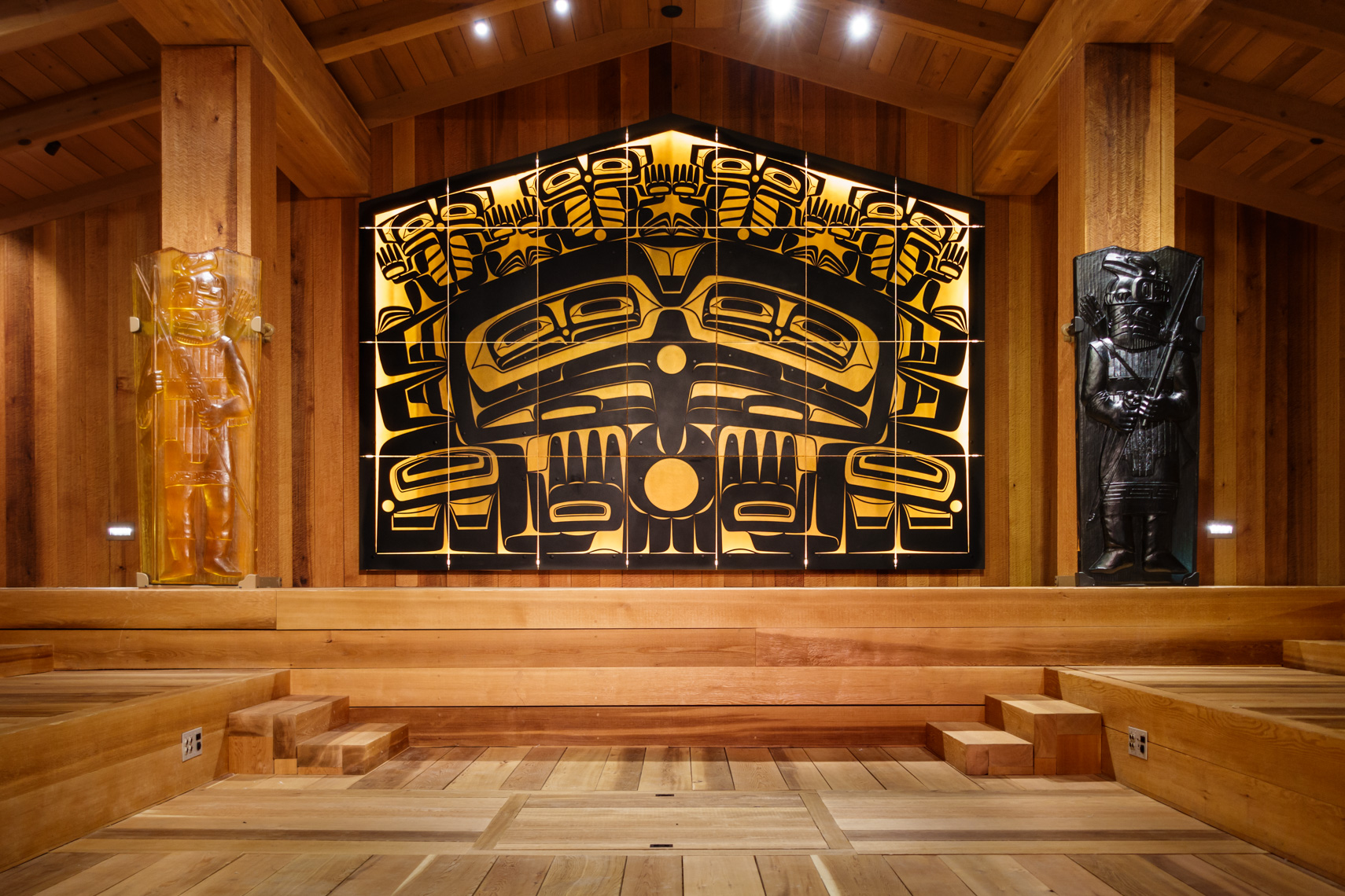 Interior of a traditional Northwest Coast Native American Indian tribal clan house, Juneau, Alaska. Glass house posts and a glass and metal screen by Tlingit artist Preston Singletary, in a typical formline art style, represent people, animals and supernatural beings.